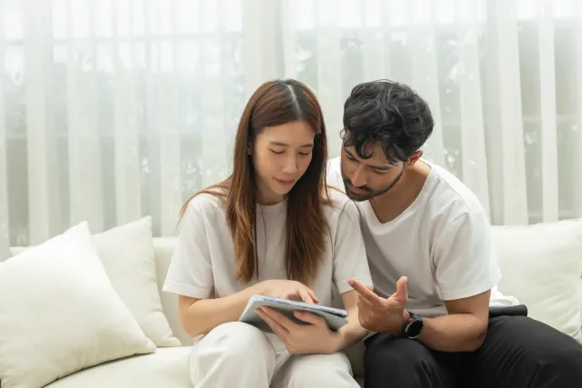 A couple reviews a tablet while sitting on a sofa.