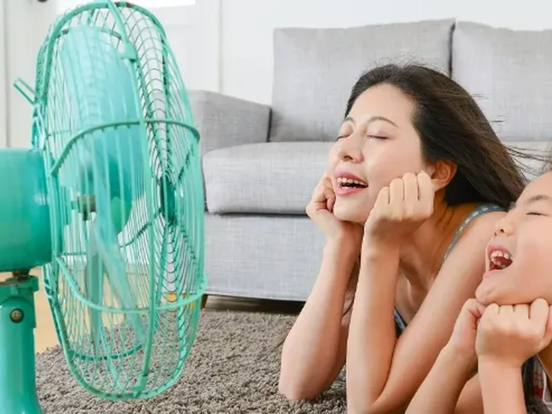 A parent and child enjoy the airflow from an electric fan at home.