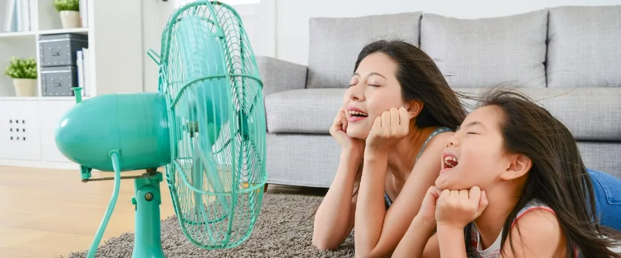 A parent and child enjoy the airflow from an electric fan at home.