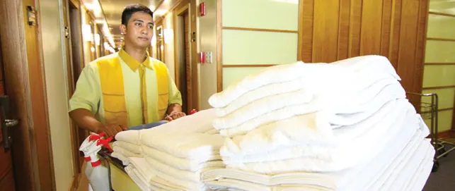 Hotel worker carries folded white linens.
