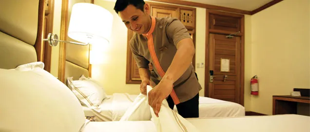 Hotel worker prepares a bed with fresh linens.