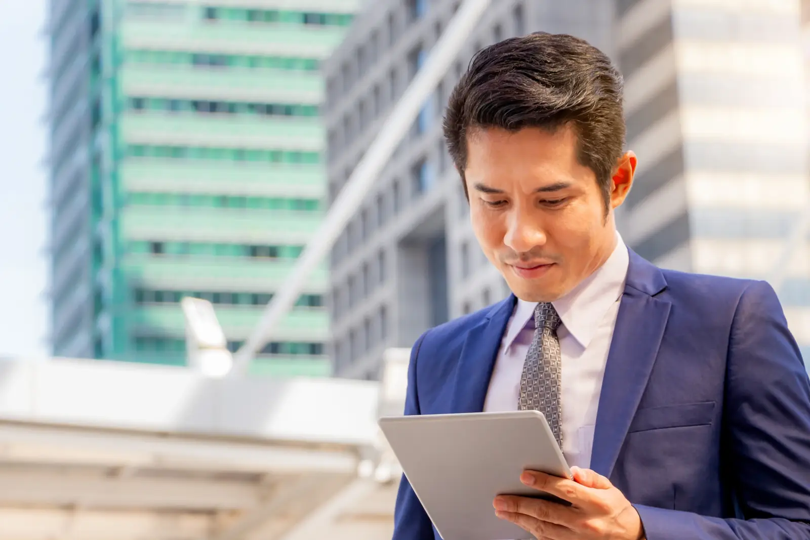 A man in a suit uses a tablet outdoors.
