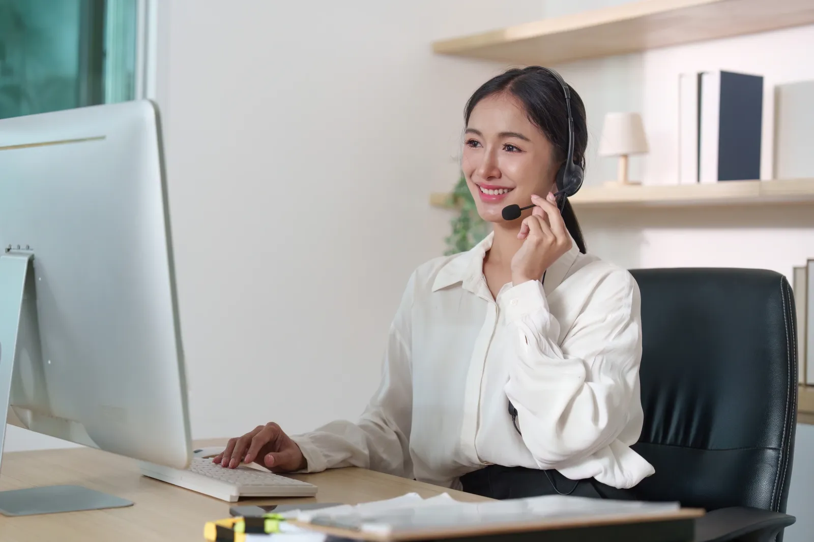 A woman wearing a headset works at a computer.