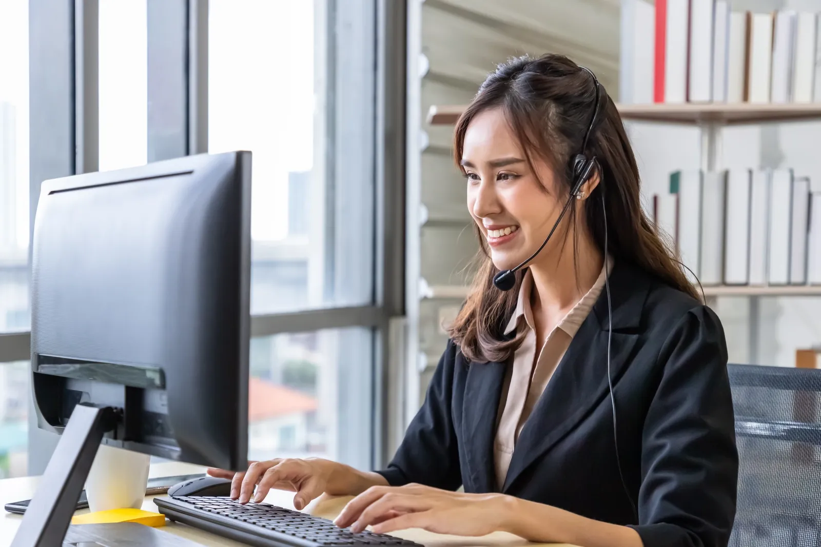 A woman wearing a headset works at a computer.