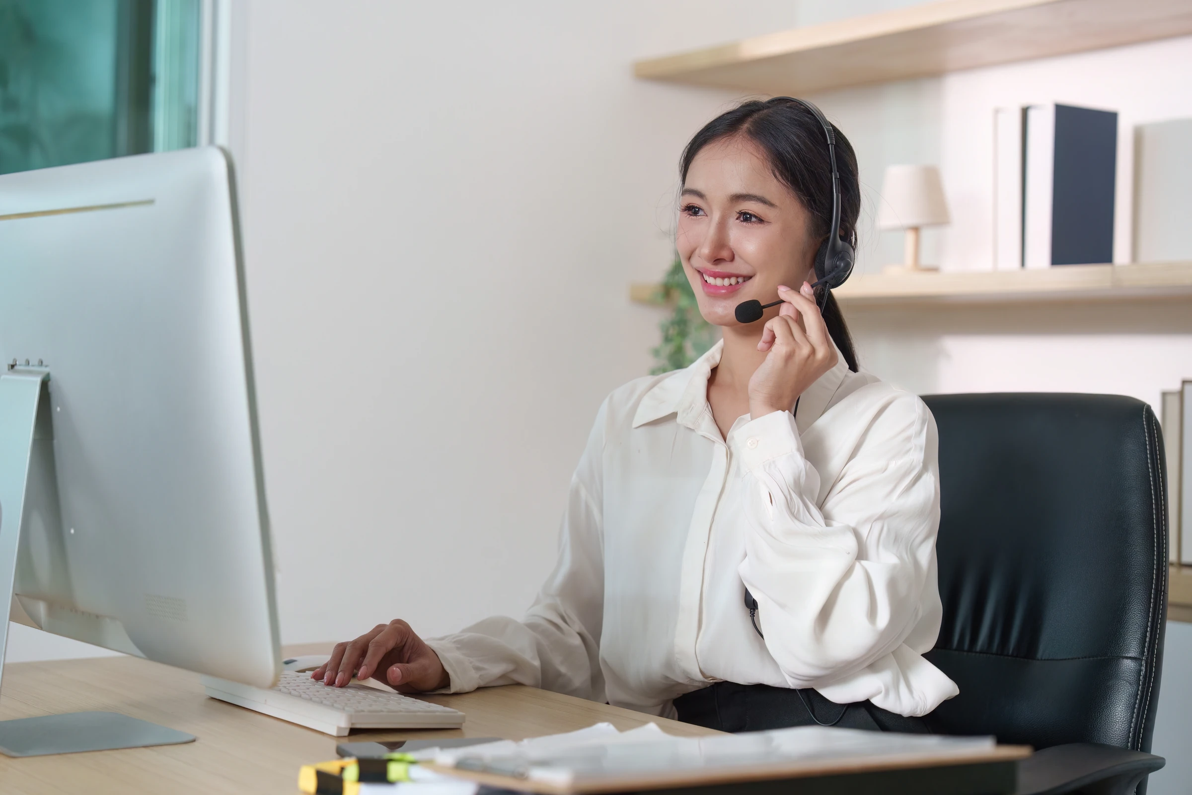 A woman wearing a headset works at a computer.