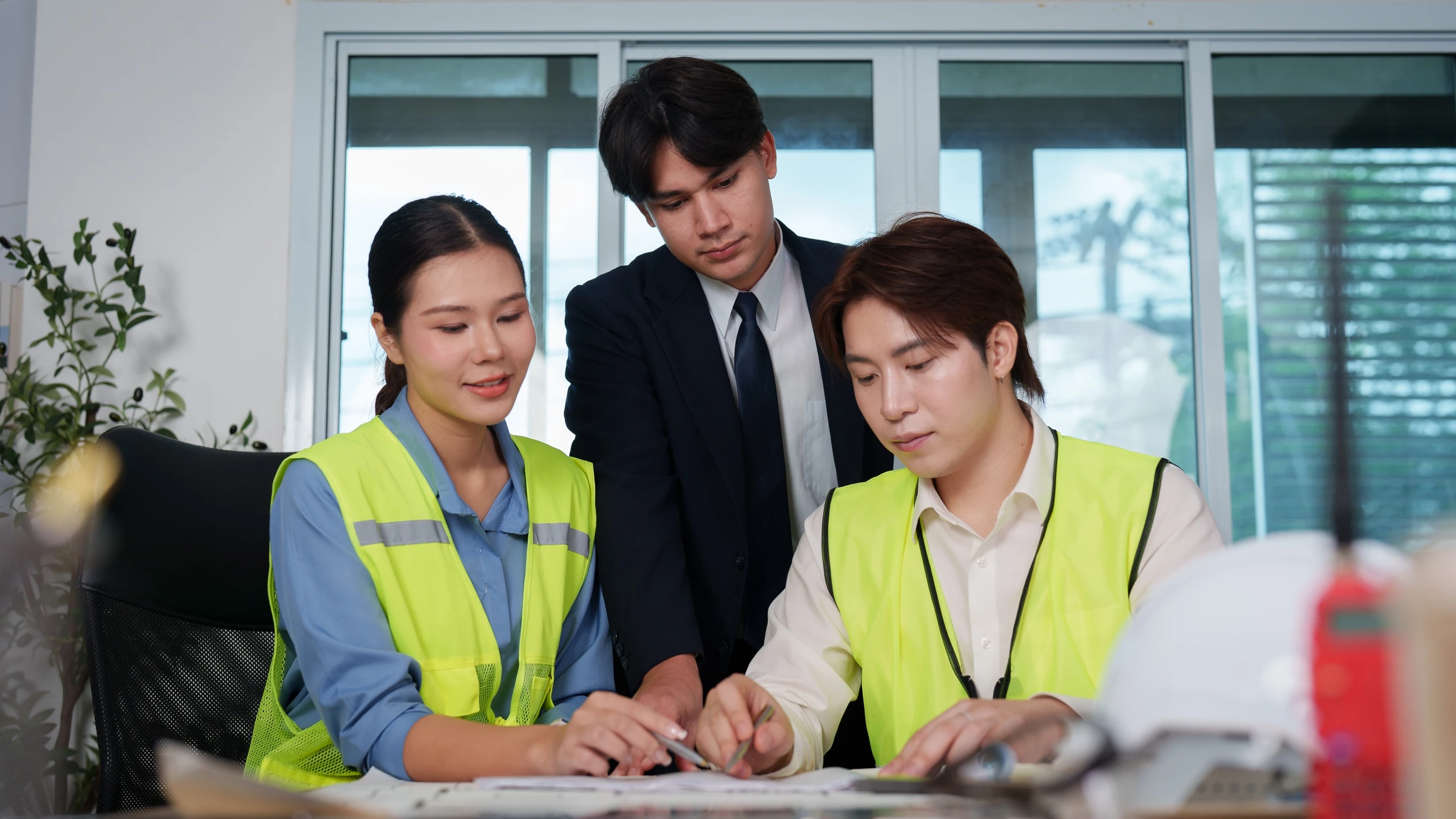 Three colleagues review documents, with two wearing safety vests.