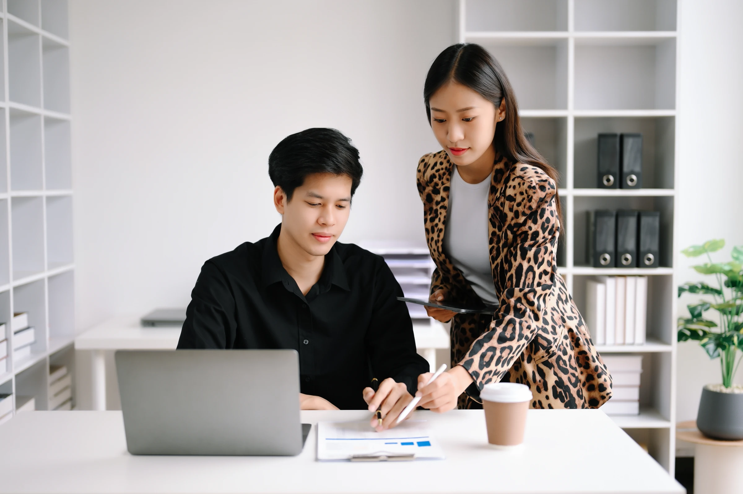 Two colleagues review documents beside a laptop.