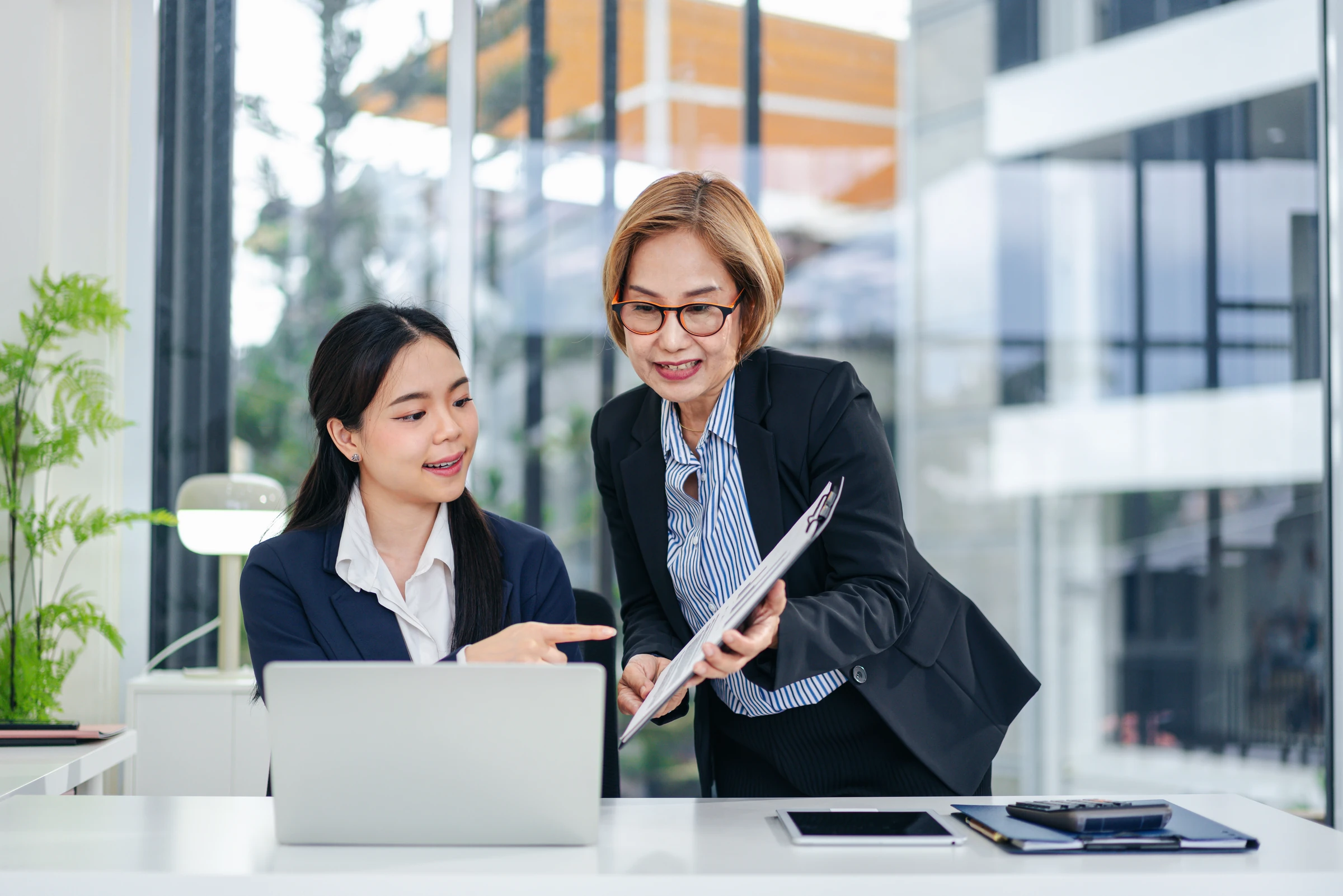 Two colleagues discuss documents at an office desk.