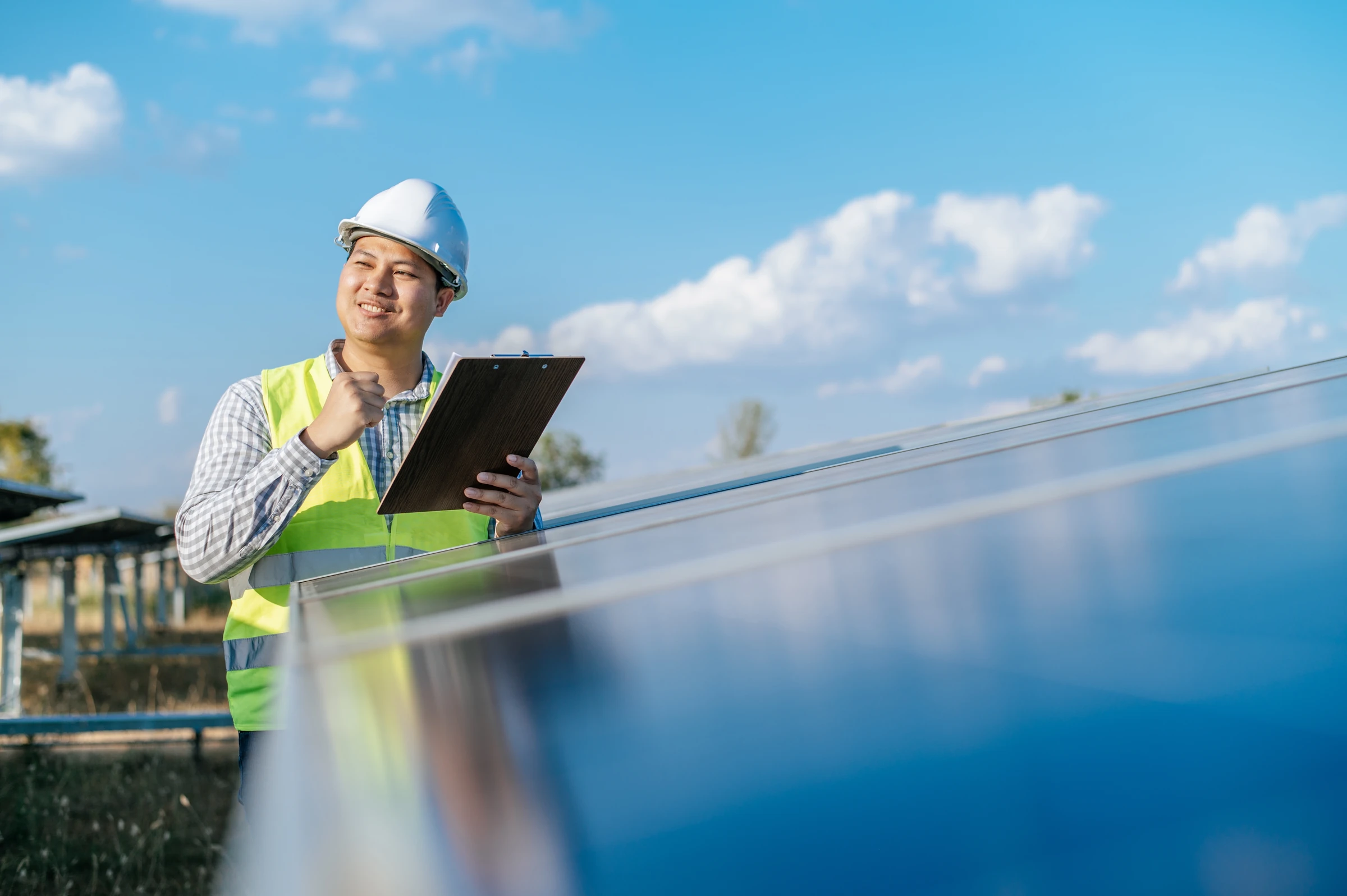 A worker in a hard hat uses a tablet beside solar panels.