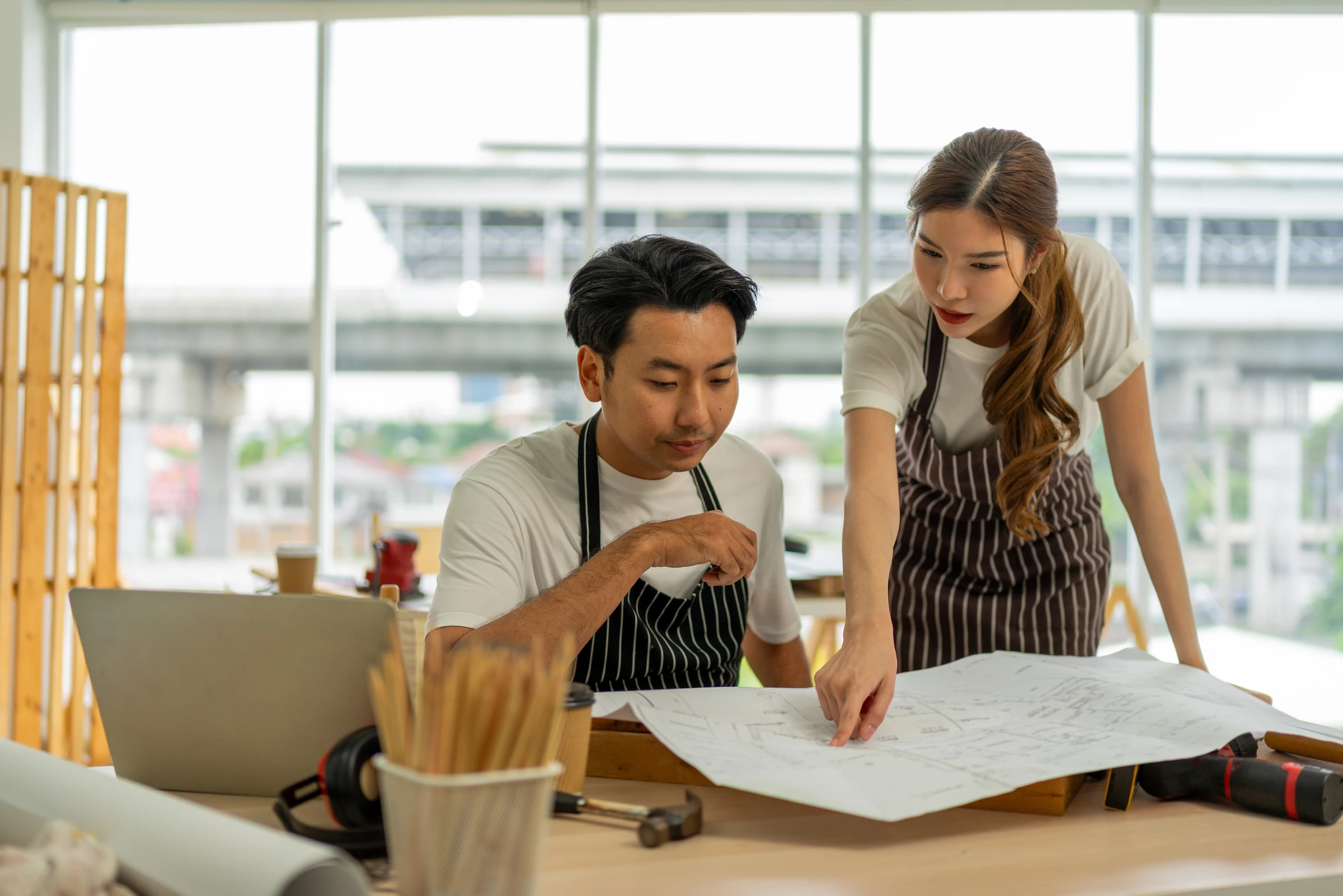 Two people wearing aprons review plans at a worktable.