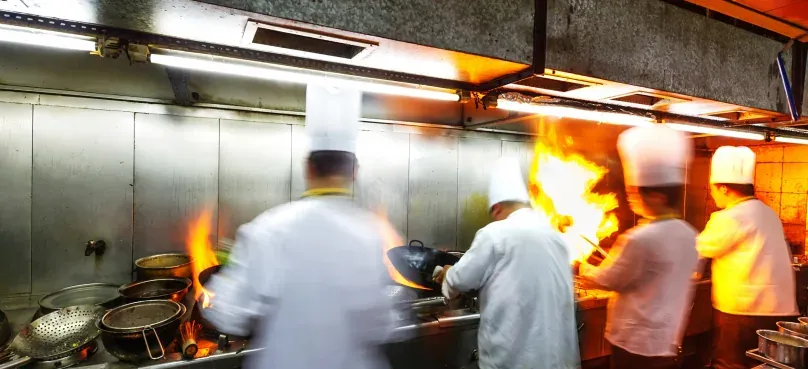 Chefs cooking over open flames in a busy commercial kitchen