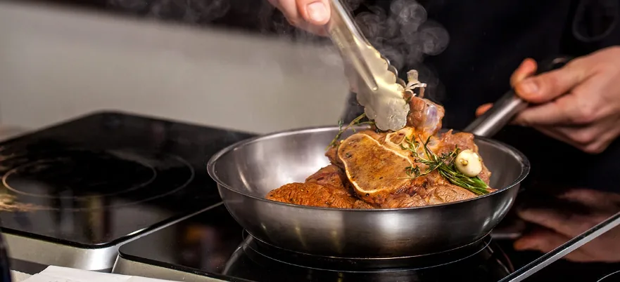 A chef cooking steak in a pan on an induction cooktop