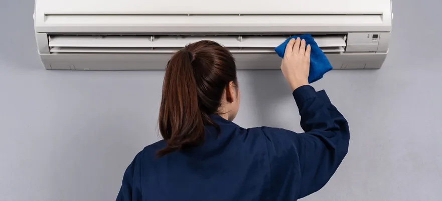 A staff member cleaning a wall-mounted split-type air conditioner