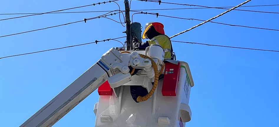 A Meralco lineworker in protective gear working on overhead power lines from a bucket truck