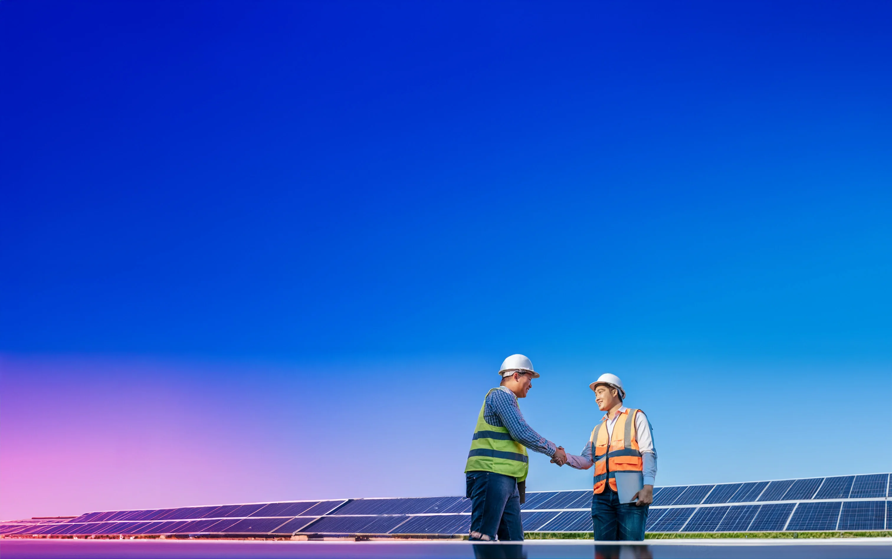 Two Meralco energy professionals shake hands in front of a solar installation.