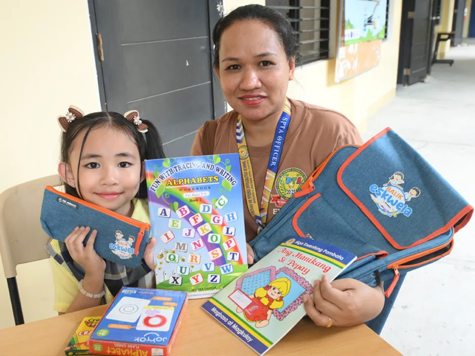 A student and teacher holding learning materials distributed through Balik Eskwela.