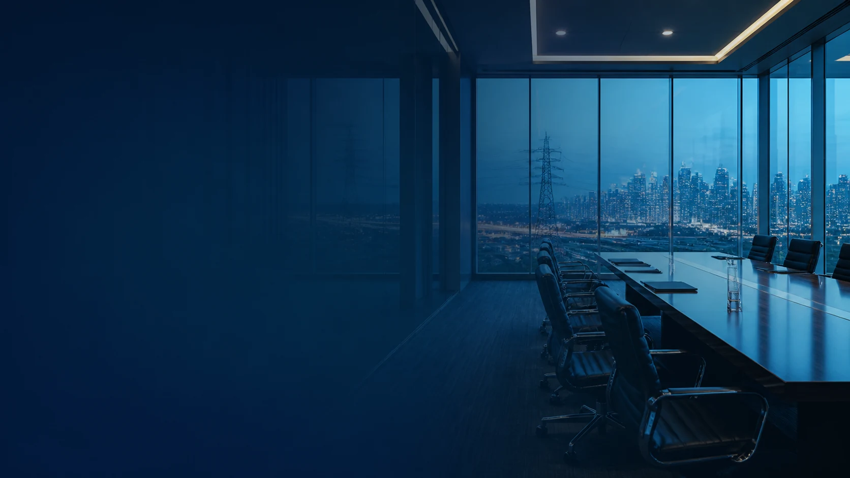 An empty executive boardroom overlooking a city and power lines at blue hour.