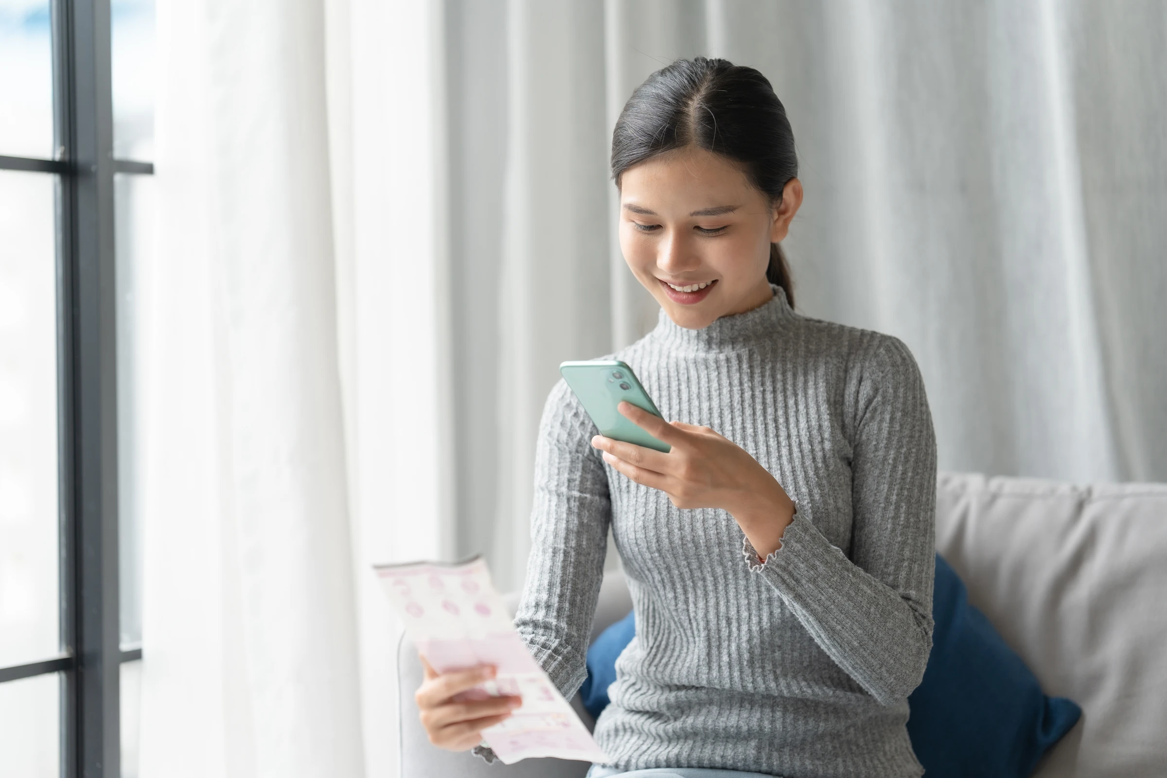 A woman uses a smartphone while holding a paper document.
