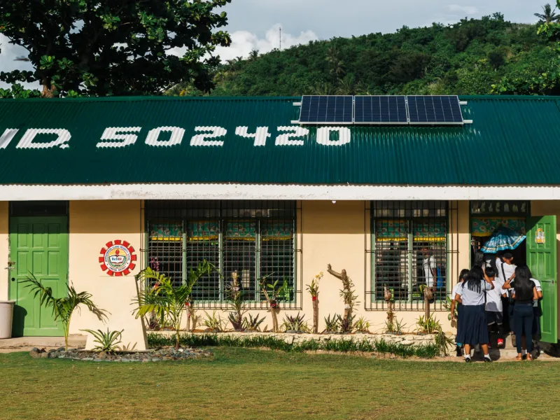 Students enter a rural school with solar panels installed on its roof.