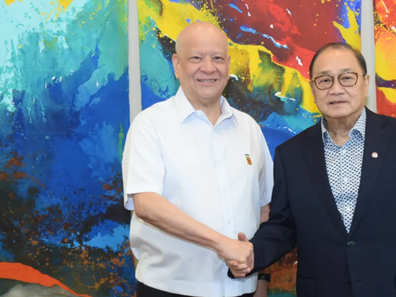 NNIC and Meralco leaders shake hands in front of a colorful painting.