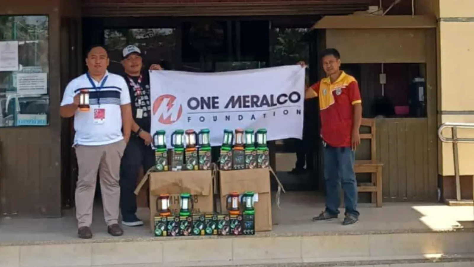 Three representatives stand behind donated solar lamps with a One Meralco Foundation banner in Masbate.