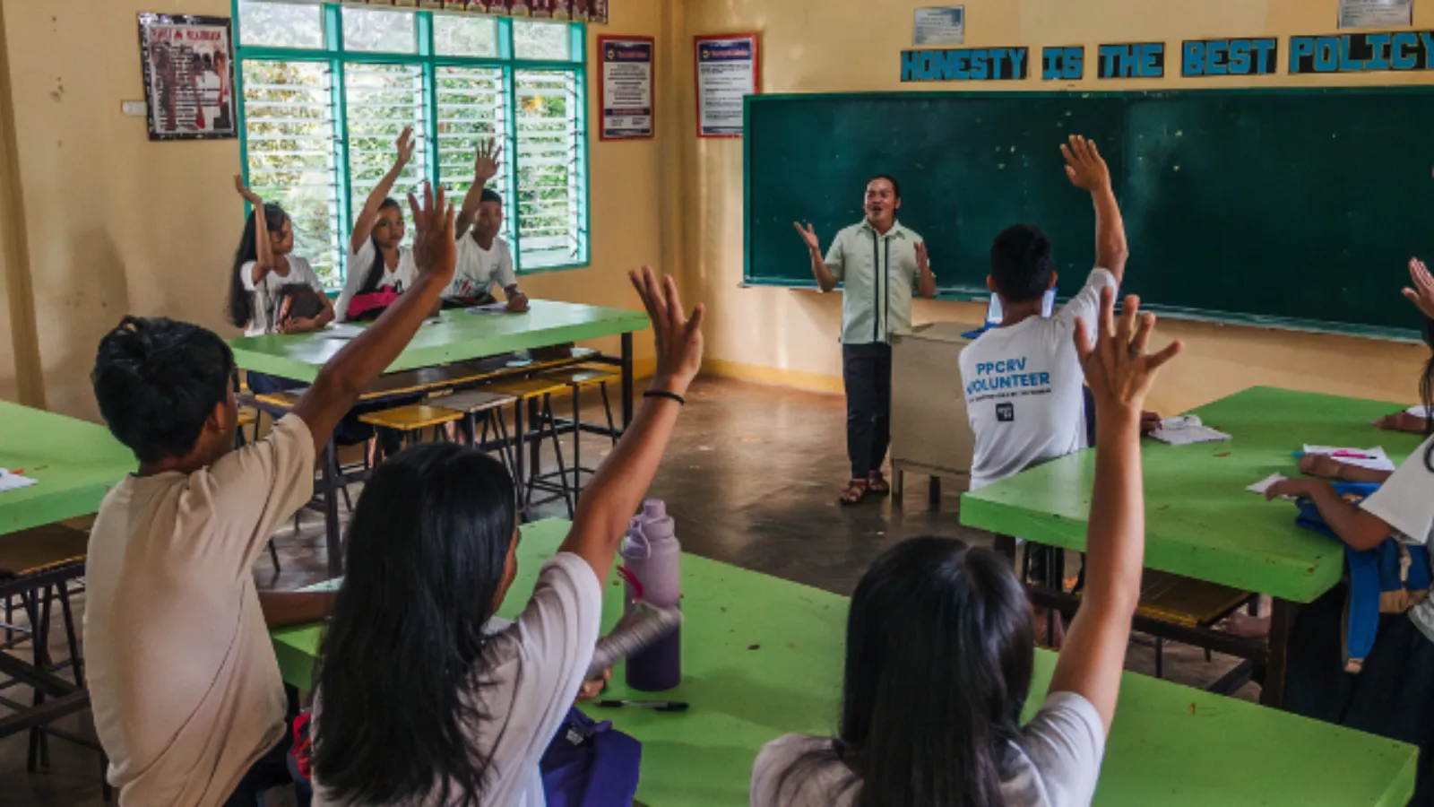 Students raise their hands while a teacher leads a class in a remote school.