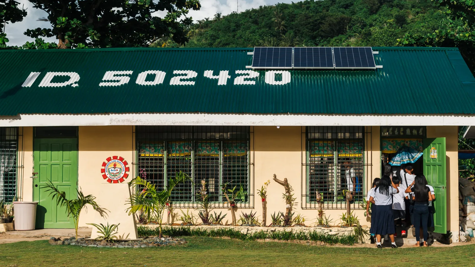 Students enter a rural school with solar panels installed on its roof.