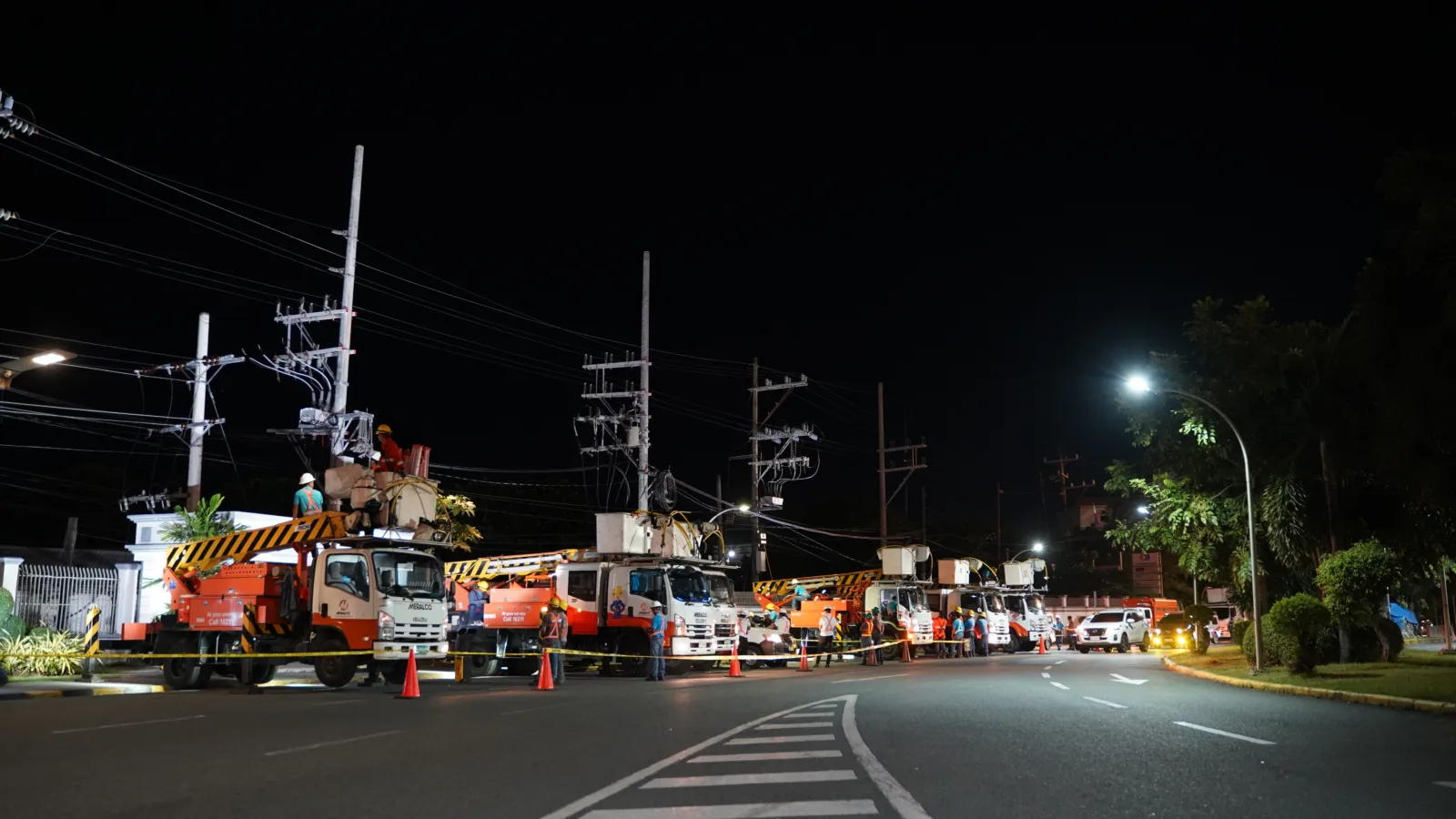 Meralco line crews in bucket trucks install power-distribution equipment for NAIA Terminals 1, 2 and 4 at night.
