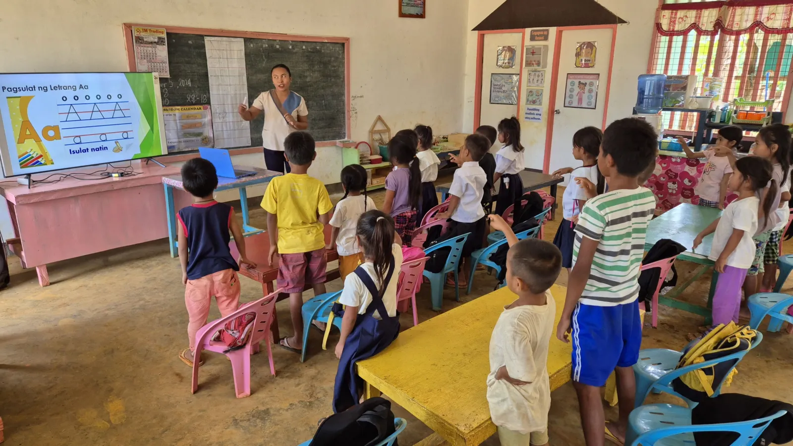 A teacher leads students through a letter-writing lesson displayed on a television at Calupisan Elementary School.