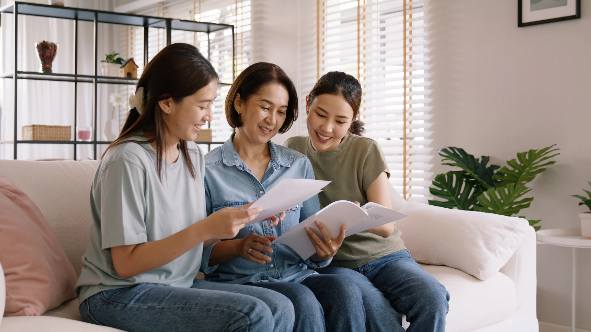 Three women review papers and a booklet on a sofa.