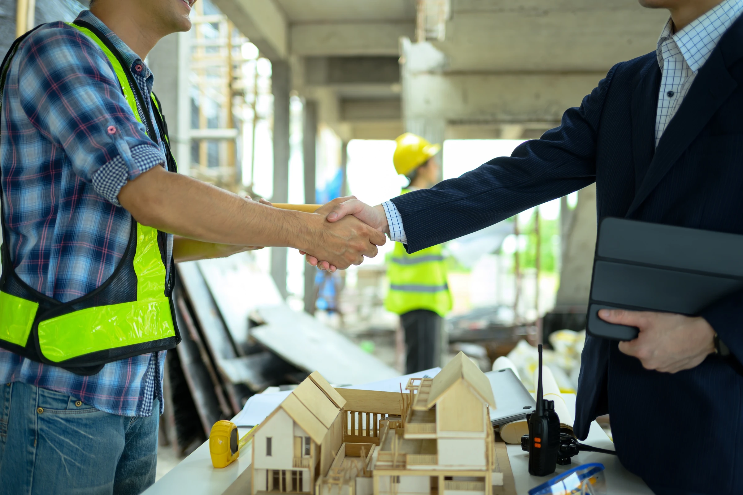 Two people shake hands over a table with an architectural model.