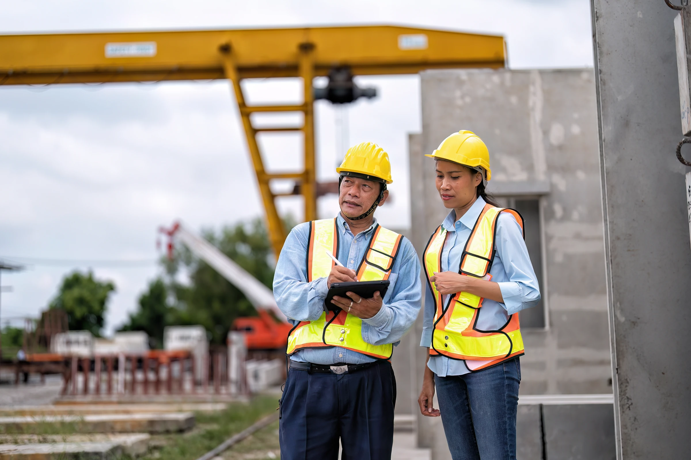 Two workers in hard hats discuss a tablet at a construction site.