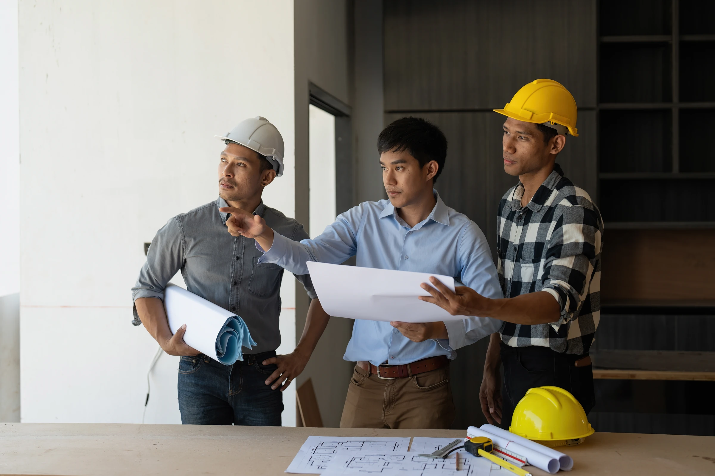 Three workers review building plans at a construction site.
