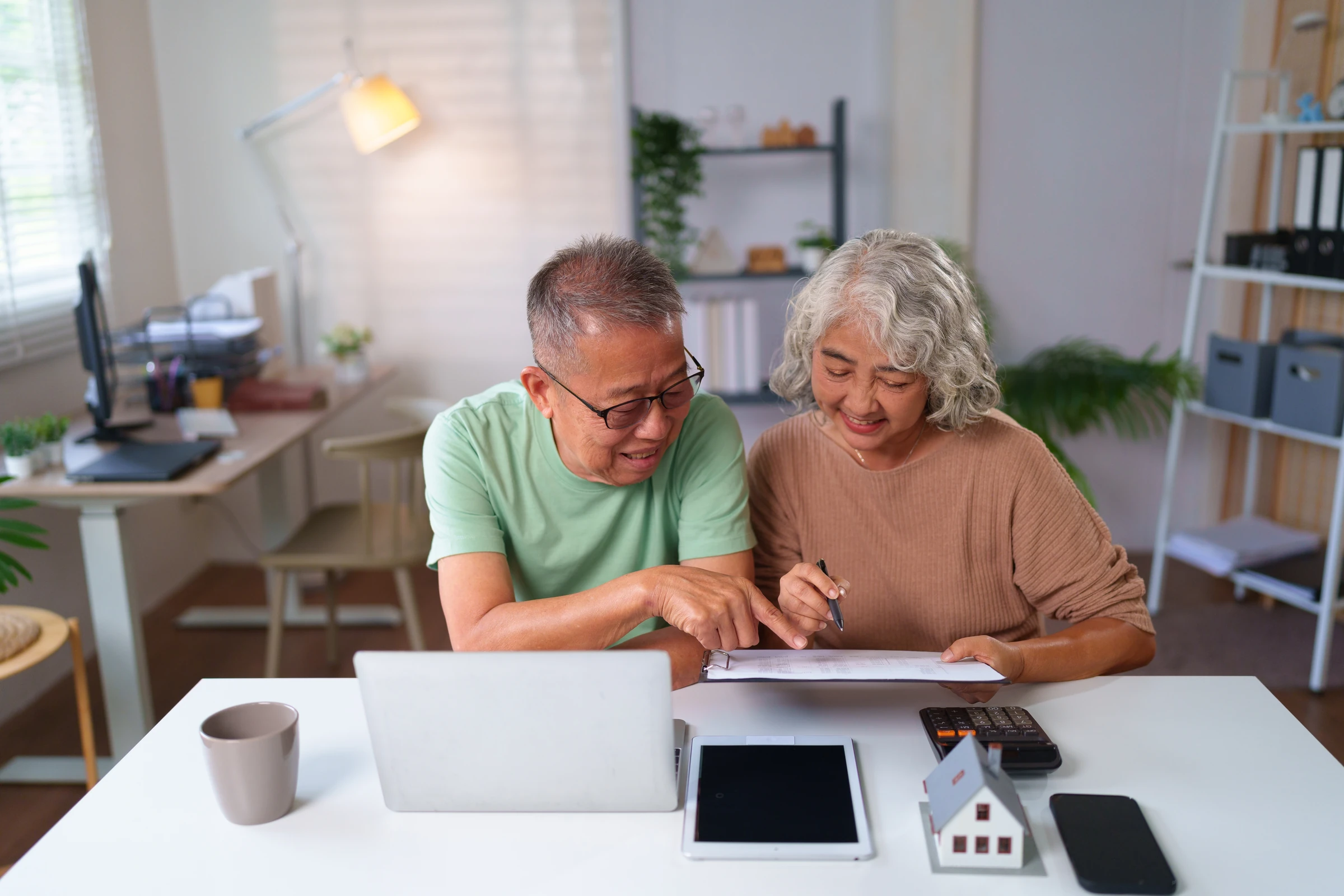 An older couple reviews documents beside a laptop.