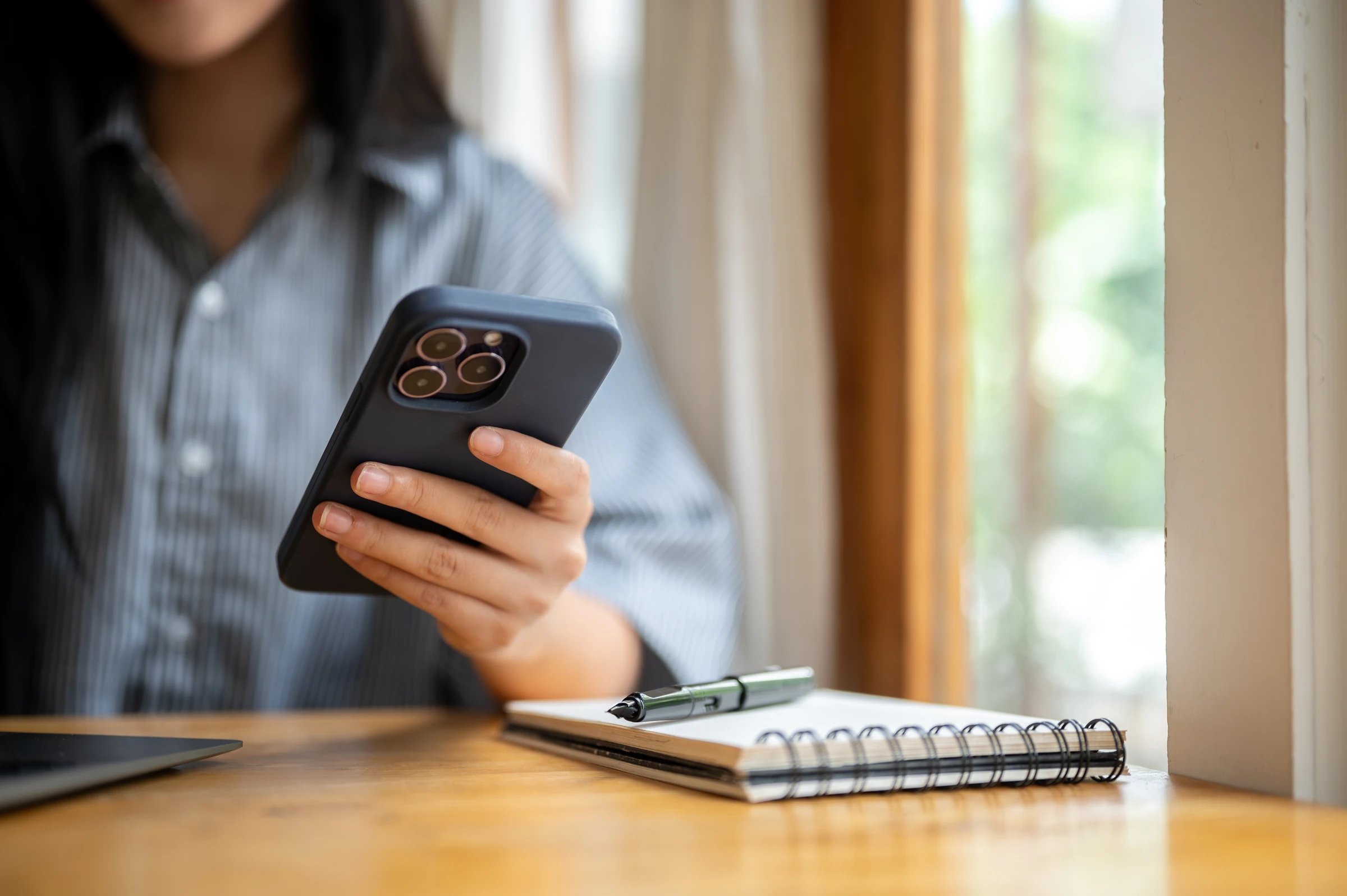 A person holds a smartphone beside a laptop and notebook.